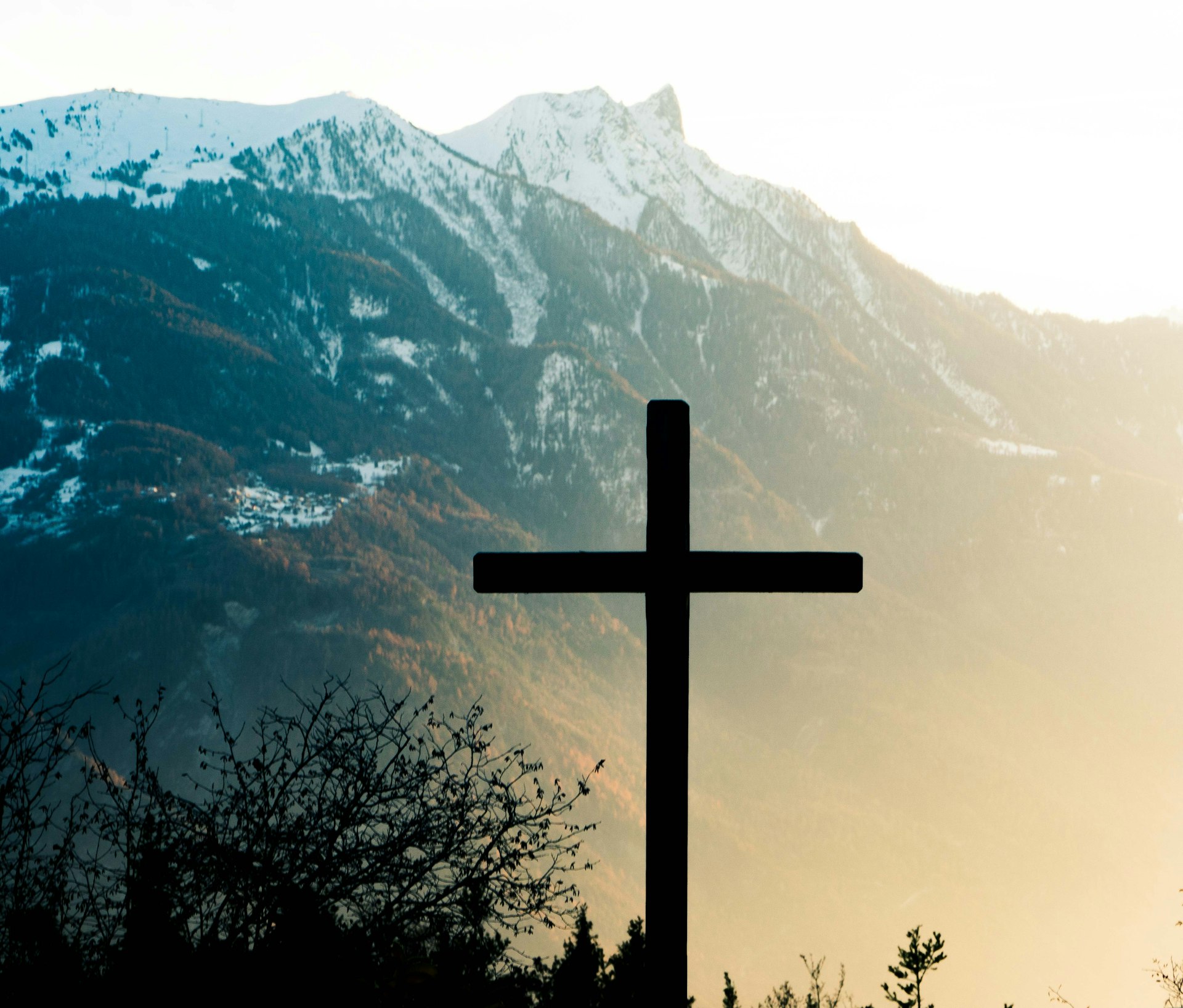 A cross silhouetted against a mountain sunset